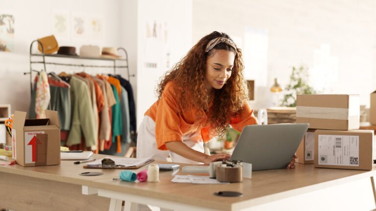 Logistics, laptop and fashion manager of retail or boutique shop checking clothing stock in boxes on a checklist. Small business, entrepreneur and young woman working with clothes inventory in store