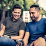 Young gay couple using mobile phones outdoors
