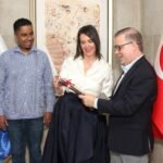 Al centro, Emriye Bağdagül Ormancı mientras hace entrega a Joan Ferrer del catálogo Antes y después de Piri Reis. Observa a la izquierda, Eliezer Nolasco director del Museo Faro a Colón.